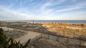 A beach with a sandy path and wooden fences, leading to the ocean.