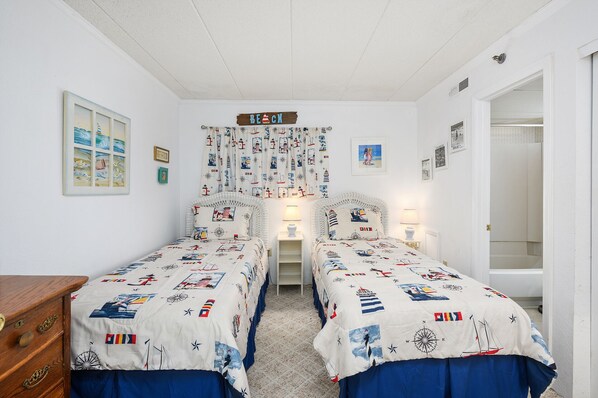 Un dormitorio con dos camas, ropa de cama con motivos náuticos, un reloj de pared y varias fotografías enmarcadas.