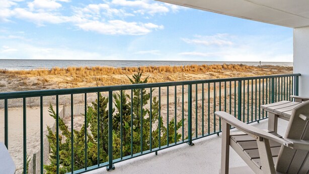 A balcony with a view of the beach, a wooden chair, and a metal railing.