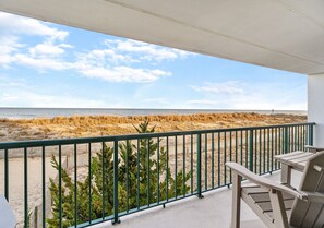 Un balcón con vista a la playa, una silla de madera y una barandilla de metal.