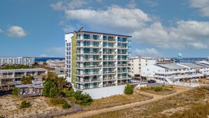 Ein mehrstöckiges Hotel mit Balkonen, gelegen in Strandnähe mit sandigem Gelände und blauem Himmel.