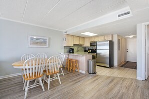 A compact kitchen with a dining area, featuring a wooden table and chairs, a stainless steel refrigerator, and a microwave.