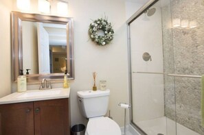 A bathroom with a mirror, sink, toilet, and a glass shower enclosure.