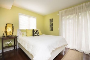 Un dormitorio con cama, mesita de noche, lámpara y ventana con cortinas.