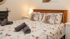 Una cama bien hecha con ropa de cama floral, un cabecero de madera y un cuadro de una vaca en la pared.