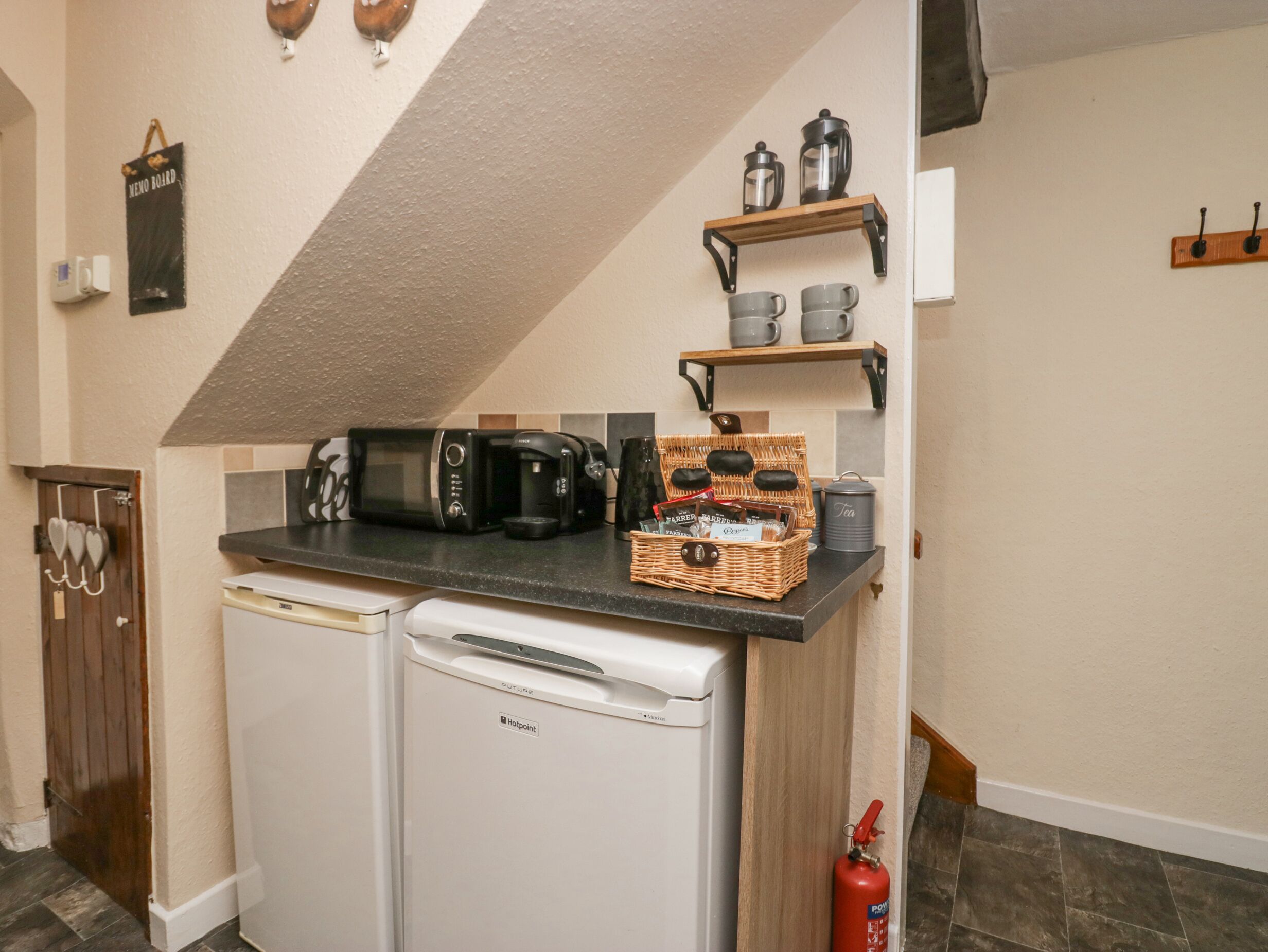 A compact kitchen with a built-in dishwasher, a coffee maker, and a wicker basket with tea bags.