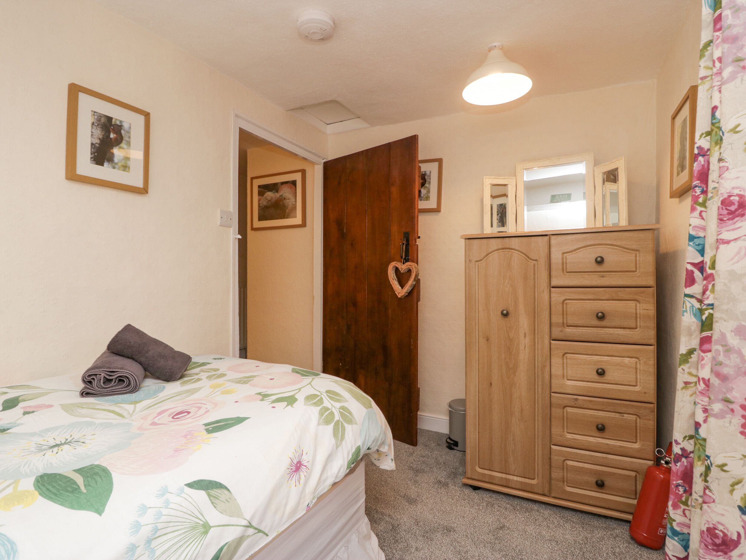 A bedroom with a bed, a wooden wardrobe, a mirror, and a door with a heart-shaped decoration.