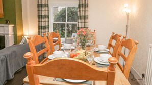 Comedor con una mesa dispuesta para cuatro, sillas de madera, un florero con flores y vistas al exterior a través de una ventana con cortinas.