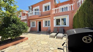 A two-story building with a stone patio, outdoor seating, and a barbecue grill.