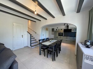 A dining area with a table and chairs, a kitchen in the background, and a staircase leading to another level.