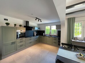 A modern kitchen with light green cabinets, a built-in oven, and a dining area with a table and chairs.