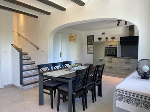A dining area with a table and chairs, a kitchen in the background, and a staircase.