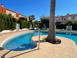A swimming pool with a tiled edge, a metal ladder, and a tree in the foreground.