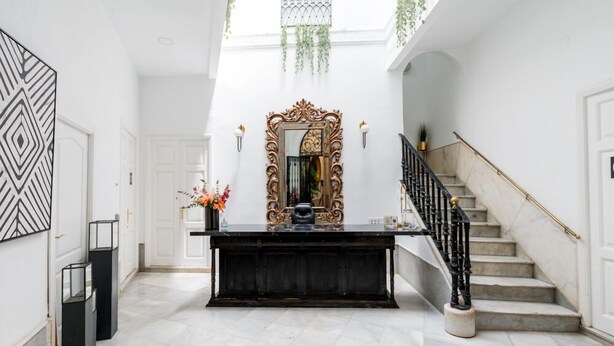 A grand foyer with a marble staircase, a large ornate mirror, and a black console table.