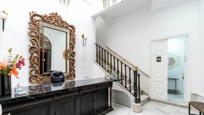 A spacious foyer with a grand staircase, a large ornate mirror, and a marble floor.