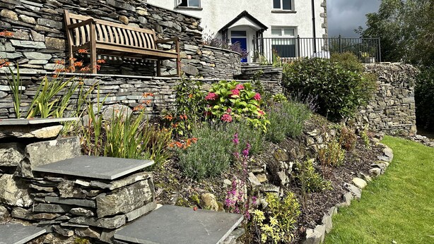 A stone house with a garden, a bench, and a blue door.
