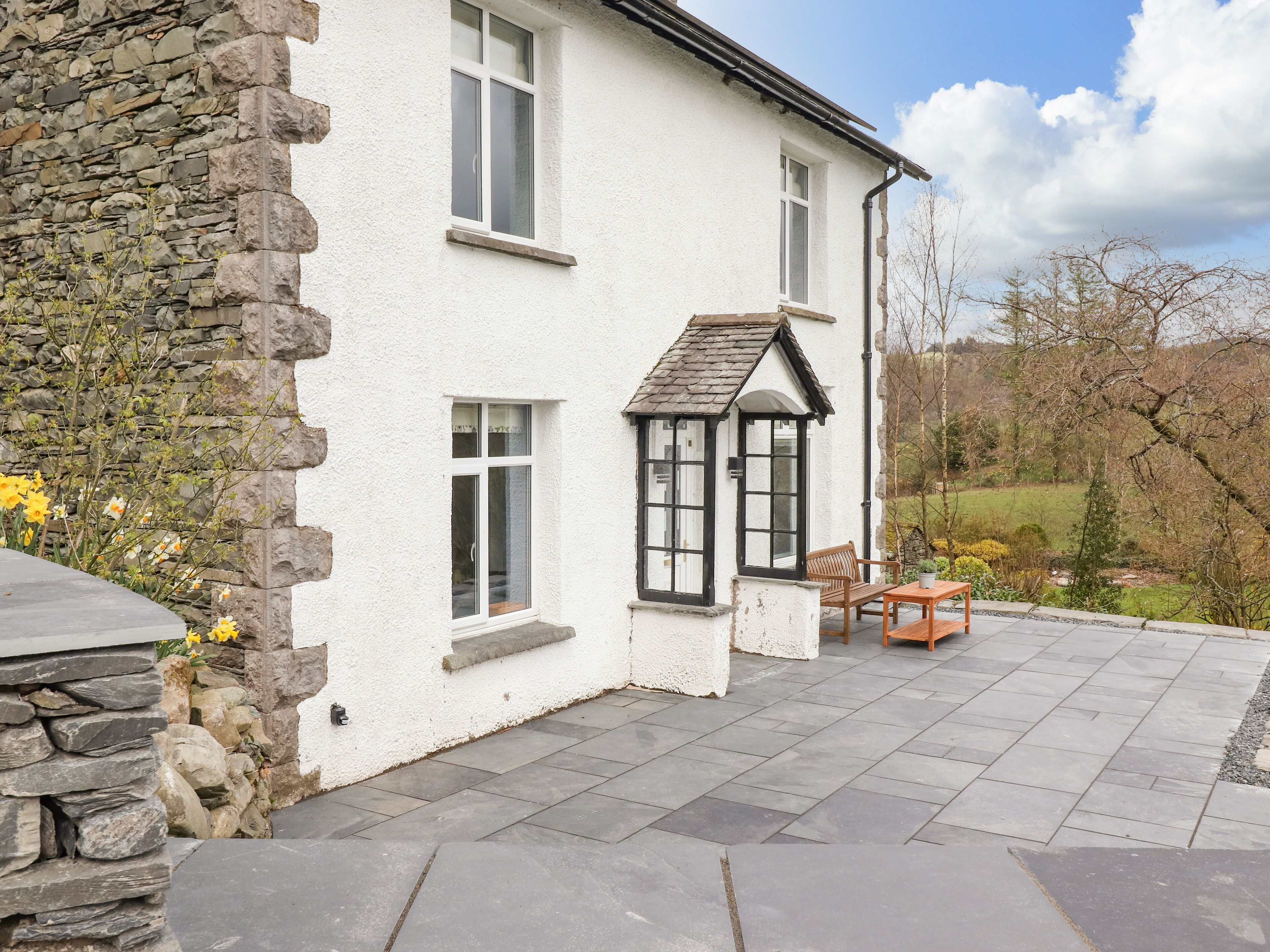 A white building with stone walls, a stone bench, and a table outside.