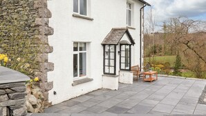 A white building with stone walls, a stone bench, and a table outside.