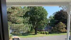 Eine Veranda mit Blick auf eine Auffahrt, ein geparktes Fahrzeug und einen großen Baum.