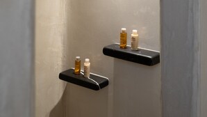 Een smalle, boogvormige douche met een lamp erboven en twee zwarte planken met flessen.