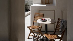 Een kleine, lichte kamer met een ronde tafel, twee houten stoelen en een hanglamp.