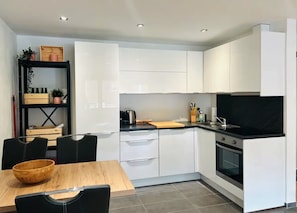 A modern kitchen with white cabinets, a black countertop, and a wooden dining table with chairs.