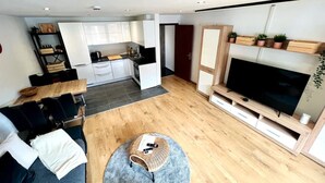 Un salon moderne avec un téléviseur, un canapé et une table basse. Il y a également un coin cuisine avec des placards et une table à manger.