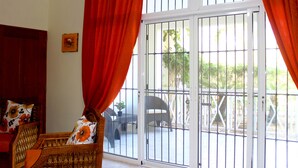 Una habitación con puerta de vidrio corredera que da a un espacio exterior, una silla de mimbre con cojines estampados y un armario de madera.