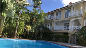 Una piscina rodeada de exuberante vegetación tropical y un edificio de varios pisos con balcones.