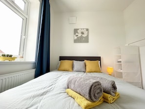 A neatly made bed with rolled towels, a bedside lamp, and a wall art piece.