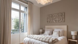 A bedroom with a large bed, two bedside lamps, a window with curtains, and a wall art piece.
