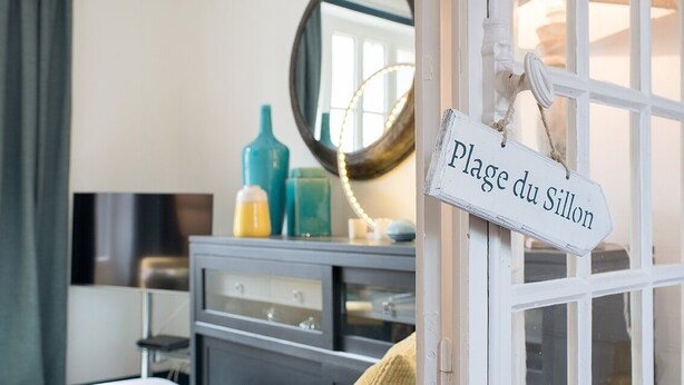 A room with a white door labeled "Plage du Sillon," a mirror, and a dresser with various items.