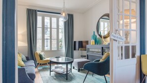 A modern living room with a sofa, armchairs, a coffee table, and a dining area with a TV and decorative items.