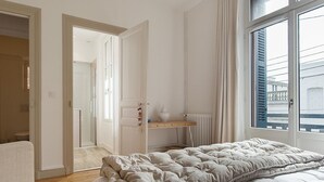 A bedroom with a bed, a window, a radiator, and a door leading to another room.