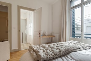 A bedroom with a bed, a window, a radiator, and a door leading to another room.