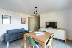 Un salon moderne comprenant un canapé, une table à manger, des chaises, un téléviseur et un coin cuisine.