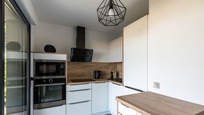 Una cocina moderna con electrodomésticos integrados, encimera de madera y una lámpara colgante de diseño geométrico.