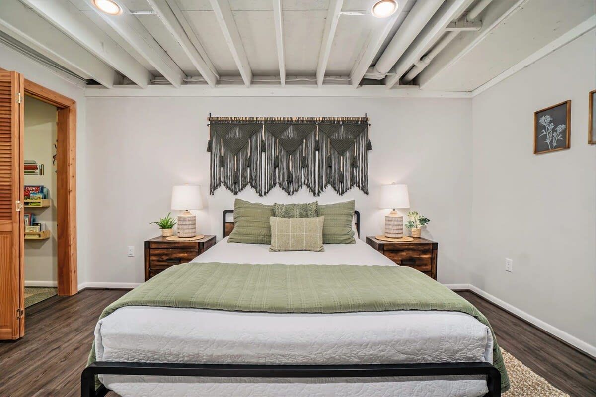 A bedroom with a bed, bedside tables, a wall tapestry, and a wooden door.