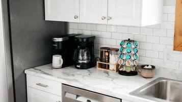 A kitchen with white cabinets, a coffee maker, a coffee pot, and a coffee machine.