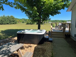 A backyard with a hot tub, a wooden deck, and a picnic table. - Hot Tub! | Pet Friendly! | Game Room! (Traverse City)