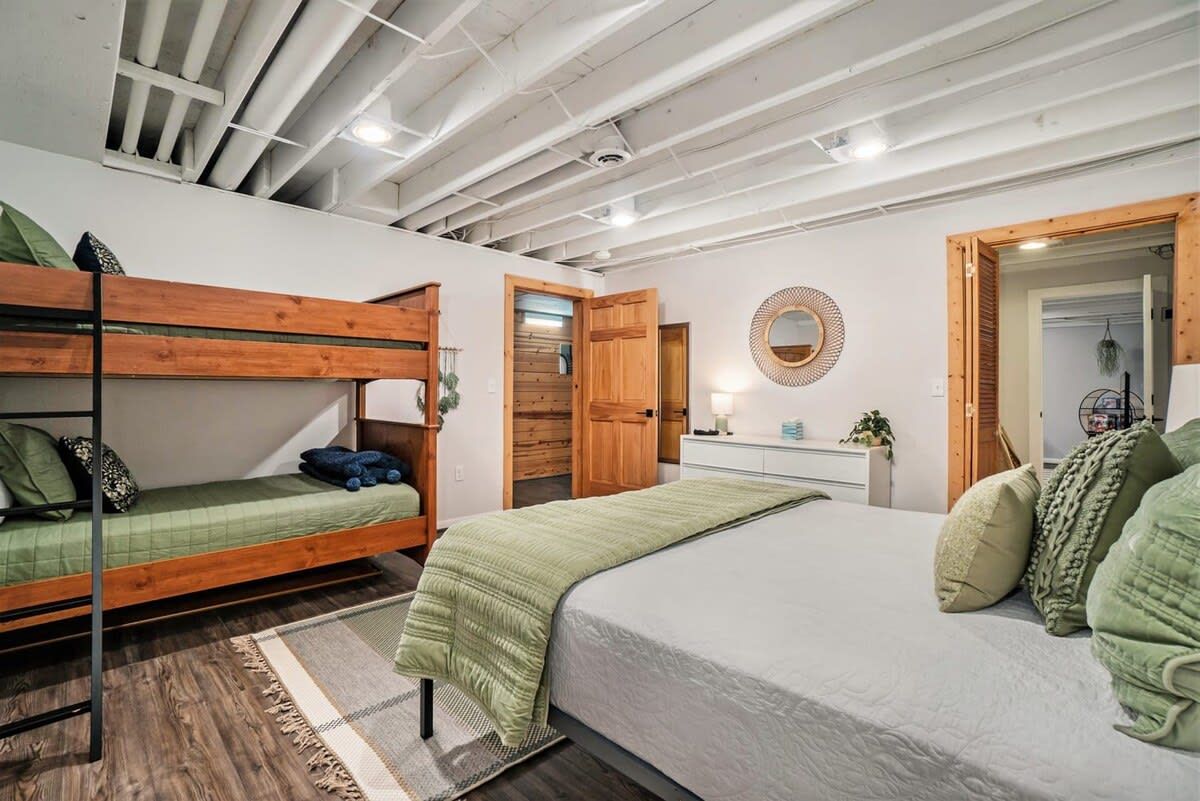 A room with bunk beds, a single bed, a bedside table with a lamp, and a mirror on the wall.