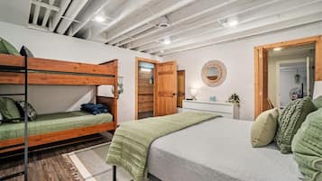 A room with bunk beds, a single bed, a bedside table with a lamp, and a mirror on the wall.