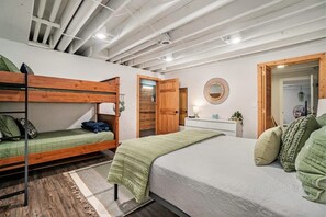 A room with bunk beds, a single bed, a bedside table with a lamp, and a mirror on the wall.