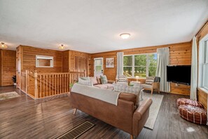 A cabin interior with a wooden interior, a sofa, a television, and a staircase. - Hot Tub! | Pet Friendly! | Game Room! (Traverse City)