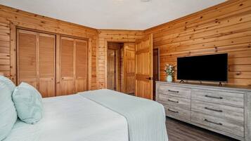 A bedroom with wooden walls, a bed with pillows, a dresser, and a television.