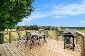 A wooden deck with a table and chairs, a grill, and a view of a green landscape.