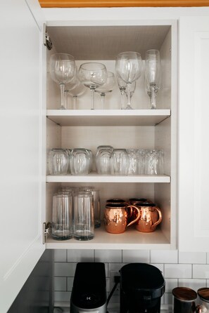 Un meuble de cuisine doté d’étagères où sont rangés des verres à vin, des bocaux en verre et des mugs en cuivre.