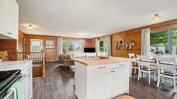 A modern kitchen with wooden walls, white cabinetry, and a dining area with white chairs and a table.