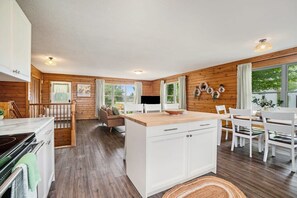 Une cuisine moderne avec des murs en bois, des armoires blanches et un îlot central. On y trouve un coin repas avec des chaises blanches et une table.
