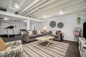 A modern living room with a treadmill, two sofas, a coffee table, and a TV stand. - Hot Tub! | Pet Friendly! | Game Room! (Traverse City)
